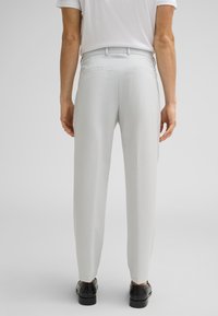 Pantalons tailleur gris clair avec une finition texturée, dotés de deux poches arrière et d'une coupe slim, associés à des chaussures noires.