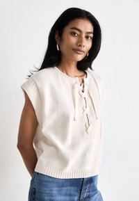 Beige knitted sleeveless top with a lace-up front, textured panels, and ribbed hem. Simple design and soft material enhance comfort.