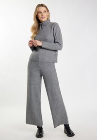 Pulover gri tricotat cu nervuri, cu guler înalt și pantaloni largi asortati. Material texturat cu o croială relaxată, combinat cu botine negre până la gleznă.