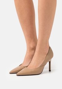 Décolleté beige in pelle con tacco alto, dalla punta affilata, design elegante e finitura testurizzata. Presenta un accento nero sul tallone.