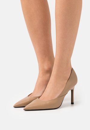Zapatos de tacón alto de cuero beige con punta afilada, diseño elegante y acabado texturizado. Presenta un acento negro en el tacón.