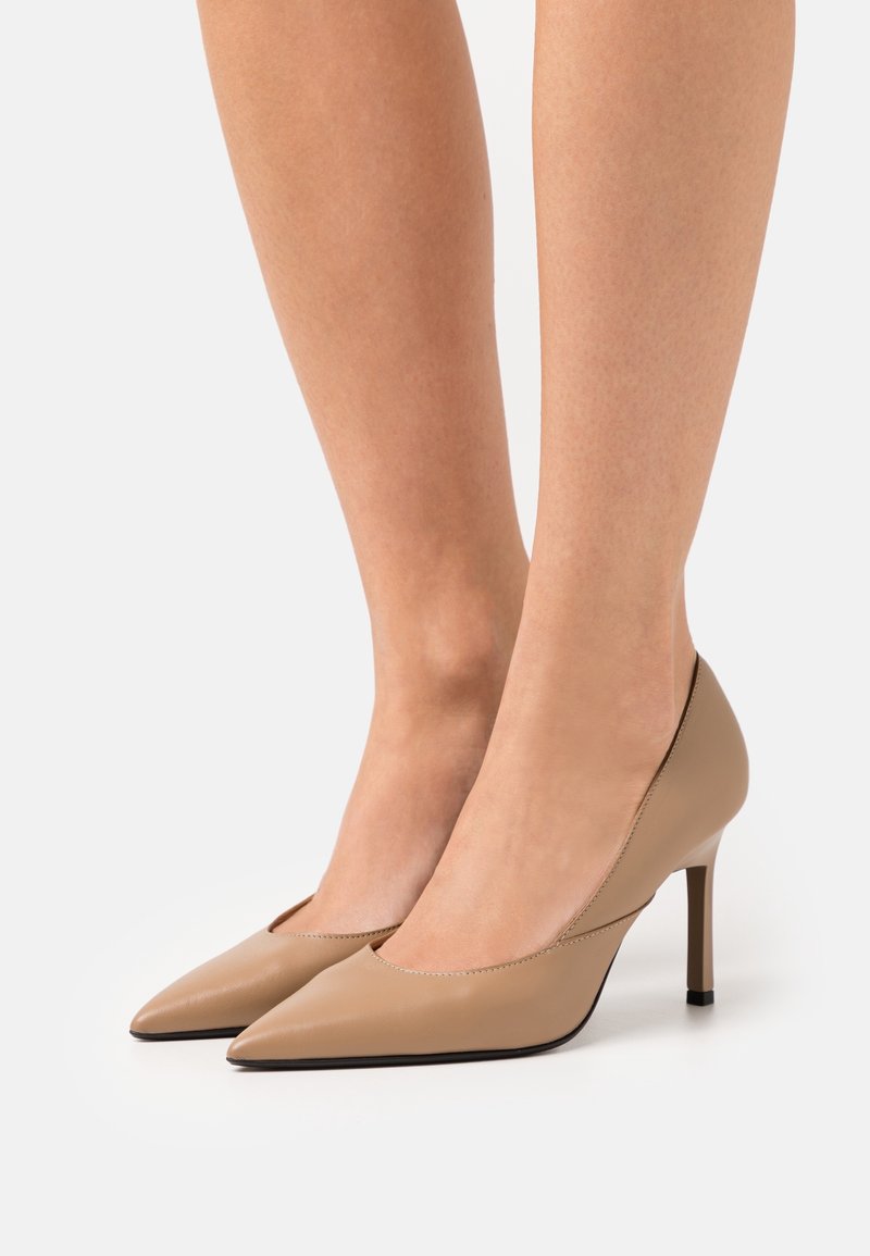 Décolleté beige in pelle con tacco alto, dalla punta affilata, design elegante e finitura testurizzata. Presenta un accento nero sul tallone.