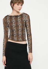 Top de manga longa em padrão leopardo, nas cores castanho e bege, com um design ajustado e decote arredondado. Combinado com uma saia preta pregueada.
