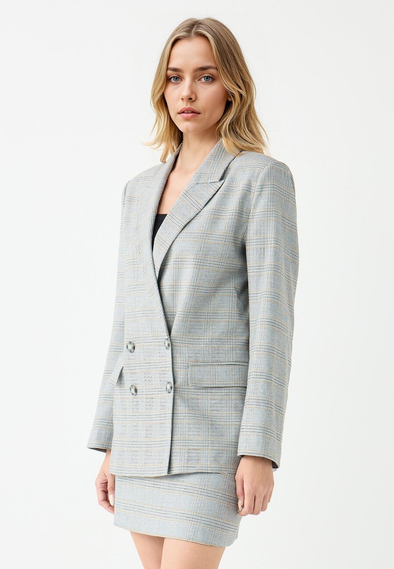 Blazer a quadri blu chiaro con doppio petto, rever a punta e due bottoni. Texture liscia, abbinato a una gonna coordinata.