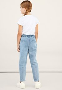 Pantaloni in denim azzurro chiaro con vita elastica, design a gamba dritta e tasche anteriori e posteriori, abbinati a una camicia bianca a maniche corte.