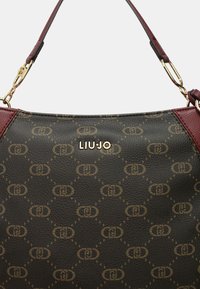 Borsa a mano in pelle marrone con dettagli vinaccia, caratterizzata da un motivo monogramma, ferrature dorate e un logo impresso sulla parte anteriore.