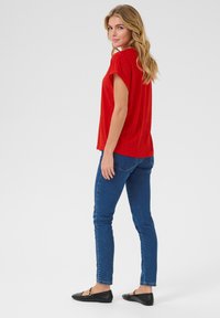 Haut rouge à manches courtes avec des détails perforés, associé à un jean skinny bleu et des ballerines noires, vu de dos.
