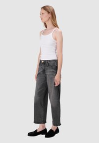 Biały prążkowany top na ramiączkach i wysokogatunkowe szare dżinsy o luźnym kroju. Czarne mokasyny z teksturowanymi akcentami dopełniają całość.