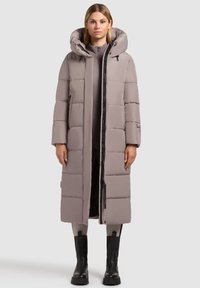 Lang, polstret frakk i lys grå med hætte, med vandrette quiltede sektioner, en frontlynlås og sidelommer. Sorte detaljer er til stede.