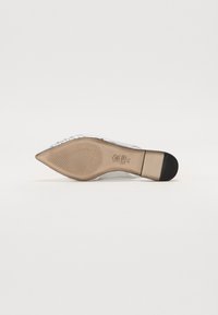 Chaussure à talon haut transparente avec un bout pointu, accents argentés, semelle intérieure texturée et un talon fin de couleur dorée. La semelle présente une texture antidérapante.
