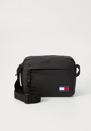 Sort rektangulær crossbody-taske med justerbar rem, lynlåslomme foran og Tommy Jeans logo i rød, hvid og blå.