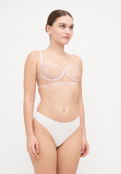 Bralette lacy rosa con copas transparentes y tirantes elásticos, combinado con braguitas de algodón blancas que presentan un pequeño detalle de lazo.