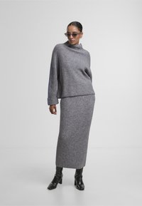 Grauer gerippter Strickpullover mit hohem Kragen und lockerer Passform, kombiniert mit einem passenden langen Rock. Getragen mit schwarzen Absatzstiefeln.