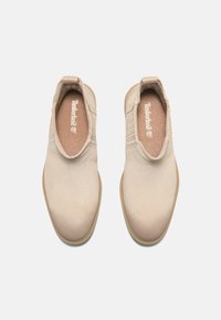 Beige Slipper mit einem glatten Wildleder-Obermaterial, elastischen Seiteneinsätzen und einer strukturierten Gummisohle. Der Markenname "Timberland" ist innen sichtbar.