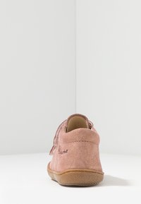 Roze suède schoen met een zachte textuur, ronde hak en tan rubberen zool. Bevat een bandje en stiksel detail bij de hak.