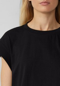 Schwarzes Baumwoll-T-Shirt mit geripptem Rundhalsausschnitt und kurzen Ärmeln, mit glatter Textur und schlichtem Design.