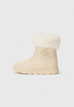 Botine bej până la gleznă cu un guler din blană sintetică, textură netedă, vârf rotund și o talpă moale cu un accent în formă de inimă pe lateral.