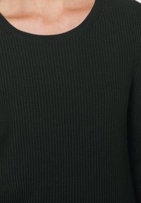 Maglione a coste verde scuro con scollatura rotonda e tessuto testurizzato, caratterizzato da un design aderente e polsini delle maniche allungati.