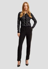 Cardigan a righe bianche e nere con scollatura rotonda e chiusura con bottoni, abbinato a pantaloni neri e decolleté nere a punta.
