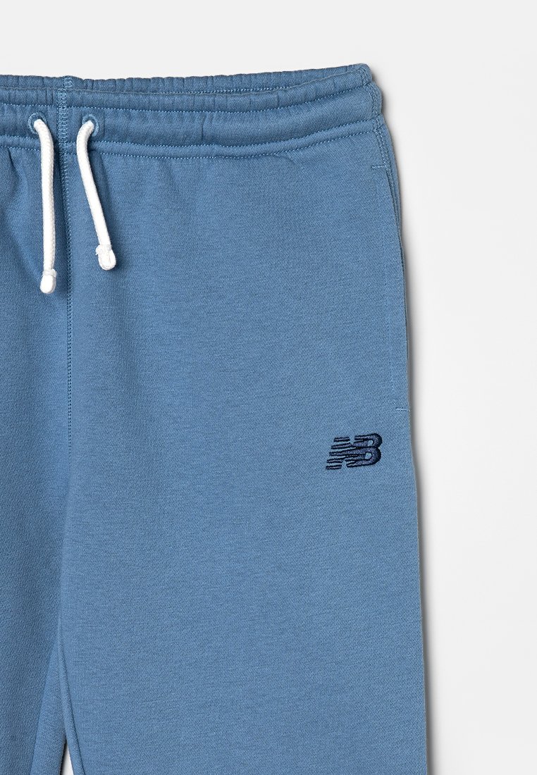 Lichtblauwe sweatpants van zacht materiaal, met een elastische tailleband en een trekkoord, en een klein marineblauw logo op het linkerpant.