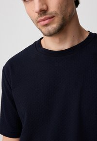 T-shirt à manches courtes bleu marine avec un motif en tricot texturé et un col rond côtelé. Tissu doux avec une coupe décontractée.