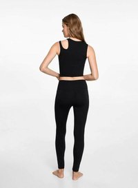 Svart croptop med ett skär i ryggen, i kombination med svarta leggings. Båda är tillverkade av ett mjukt, elastiskt material för komfort och rörelsefrihet.