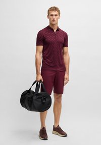 Burgundská polo košile s texturovaným vzorem, odpovídající šortky a černá kulatá sportovní taška. Hnědé sportovní boty s béžovými podrážkami.