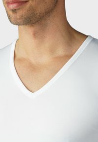 Biała koszulka typu v-neck wykonana z miękkiej tkaniny, o gładkiej fakturze i czystym, prostym wzorze. Brak widocznych wzorów lub elementów metalowych.