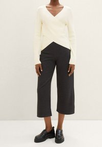 Krämfärgad ribbad långärmad topp med djup V-ringning, kombinerad med skräddarsydda mörkgrå vida cropped-byxor och svarta plattformsskor.