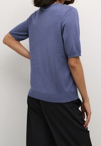 Kortærmet lyseblå strikket sweater med rund halsudskæring og ribbet kant, parret med sorte vide bukser. Glat tekstur.
