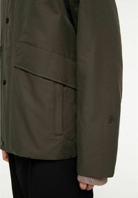 Olivgrön jacka med vattentålig finish, med framsdragkedja, stor ficka och texturerade stickade mudddetaljer. Svart logotypaccent.