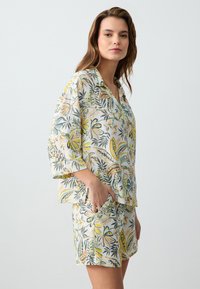 Ensemble de loungewear léger à motifs floraux en blanc, avec de grandes feuilles jaunes et vertes, des manches courtes et une coupe décontractée avec des poches.