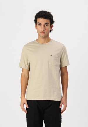 Tricou din bumbac bej cu decupaj rotund, mâneci scurte și o franzelă pe partea stângă a pieptului, având un detaliu mic al unui logo.