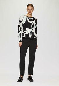 Zwarte trui met een wit en blauw bloemenontwerp, gecombineerd met zwarte, op maat gemaakte broek en zwarte loafers. Zachte textuur, ontspannen pasvorm.