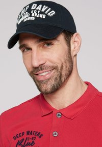 Navy cap with "CAMP DAVID" text, red polo shirt with logo and button detailing, displaying a textured fabric and collar.