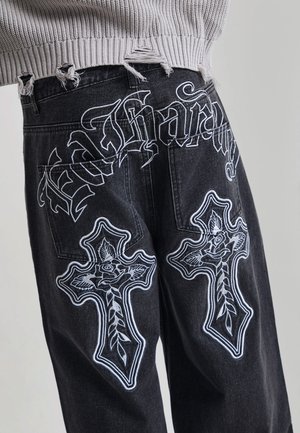 Black jeans with white embroidered crosses and floral designs on the back pockets, paired with a frayed gray knit sweater.