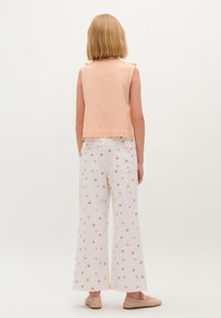 Perzikkleurige mouwloze blouse met een gaatjespatroon, gecombineerd met witte wijde broekspijpen met een multicolor bloemenpatroon en een gegolfde zoom.