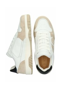 Zapatillas de cuero blanco y ante beige con punta redondeada, lengüeta acolchada y detalles negros en el talón. Suela de goma con un sutil patrón de relieve.