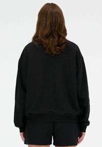 Sweatshirt noir surdimensionné en tissu doux, avec des épaules tombantes et un ourlet côtelé, assorti à un short noir pour un look décontracté.