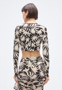 Κοντό τοπ με μακριά μανίκια, διακοσμημένο με μαύρο και μπεζ ανθικό σχέδιο, υφασμένο ύφασμα και εφαρμοστή γραμμή. Συνδυάζεται με φούστα με ρίγες σε τόνους που ταιριάζουν.