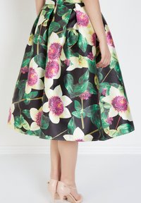 Falda floral con fondo negro, grandes flores blancas y rosas, hojas verdes y diseño plisado; combinada con tacones nude.