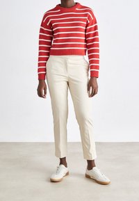Pull en tricot à rayures rouges et blanches avec un col rond associé à un pantalon beige ajusté et des baskets blanches avec des semelles en caoutchouc marron.