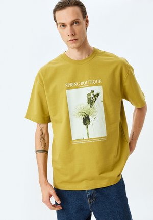 Oliven grøn bomulds t-shirt med grafisk trykke af en blomst og en sommerfugl, rund halsudskæring, korte ærmer og en løstsiddende pasform.