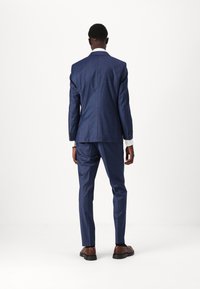 Navy blue tailored suit with a check pattern, slim fit. Features a single vent, two-button closure, and brown leather shoes.