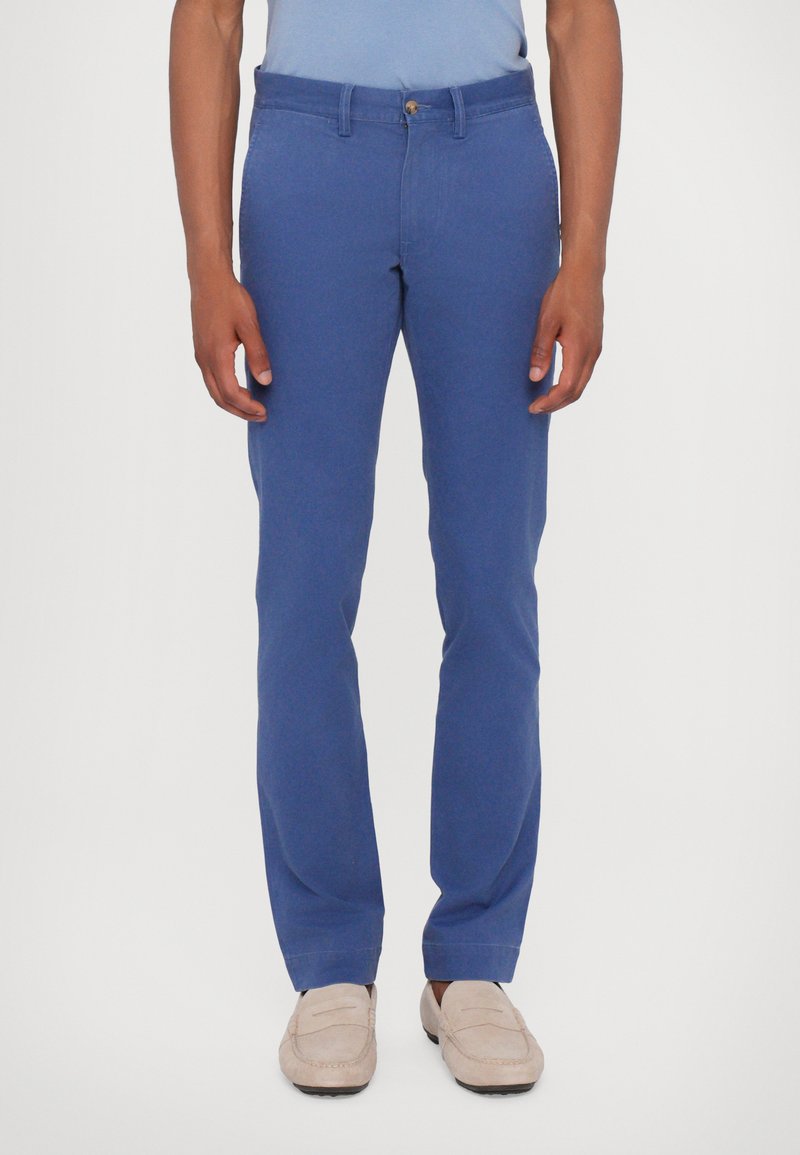 Pantaloni di cotone blu con vestibilità slim, vita media, tasche anteriori e chiusura a zip, abbinati a mocassini di colore chiaro.