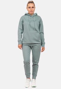 Felpa in cotone verde chiaro con tasca frontale, coulisse e polsini a coste, abbinata a pantaloni jogger coordinati con orli elasticizzati.