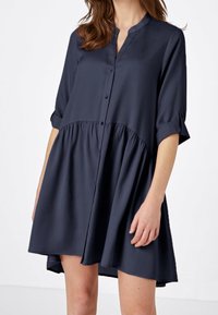 Vestido camisero azul marino hecho de tela suave, con un frente abotonado, mangas 3/4 y un diseño de falda fruncida para un ajuste relajado.