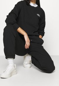 Czarny bawełniany sweter z okrągłym dekoltem i logiem, w zestawie z dopasowanymi dresami i białymi sneakersami, z elastycznymi mankietami i luźnym krojem.