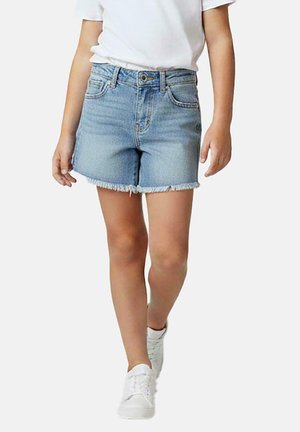 Kind draagt lichtblauwe spijkershorts met rafelige zoom, wit T-shirt en witte sneakers, loopt vooruit tegen een effen achtergrond.