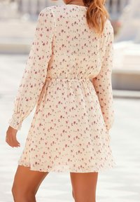 Kukkakuosiset pitkähihaiset mekko, jossa on pleatattu tekstuuri, kermaisuus pohjaväri ja joustava vyötärö. Mekossa on pieniä vaaleanpunaisia ja vihreitä kukkia.